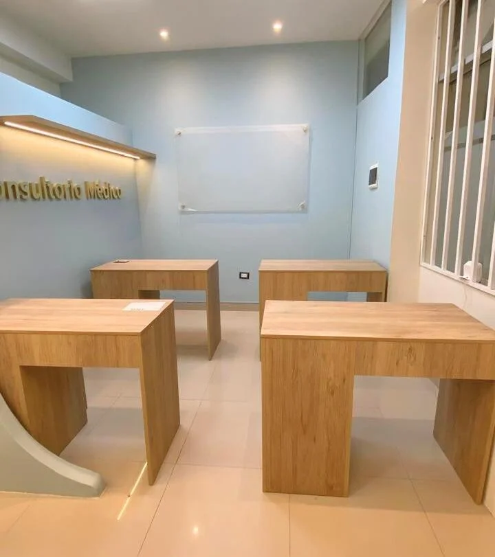 Consultorio Médico (fotografía) — sala construida con letrero dorado y mesas de madera